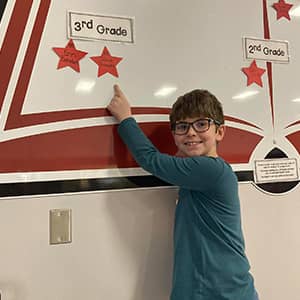 student pointing to a star under the sign reading 3rd grade