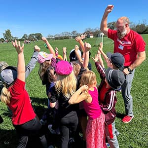 An adult with students raising the arms up