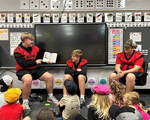 Athletes reading a book to younger students